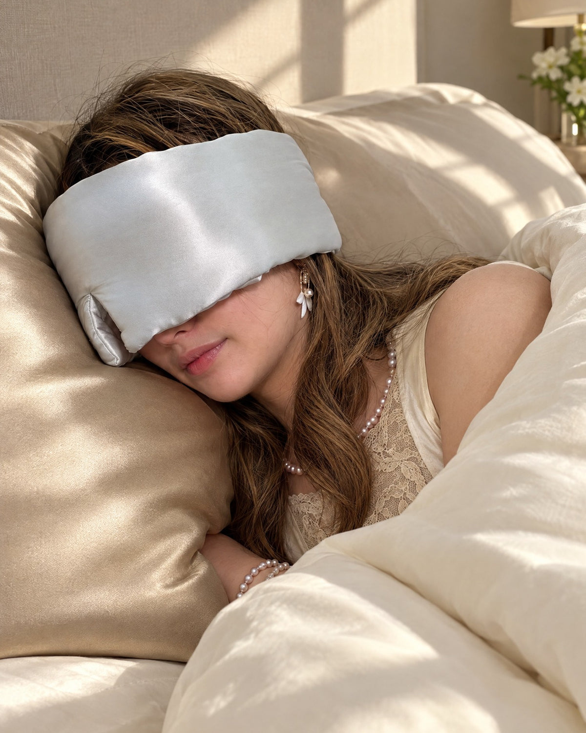 Debbie resting on the Mid9ight Dream Luxe mulberry silk pillowcase in Champagne, wearing the Deep Sleep eye mask in Moonlight