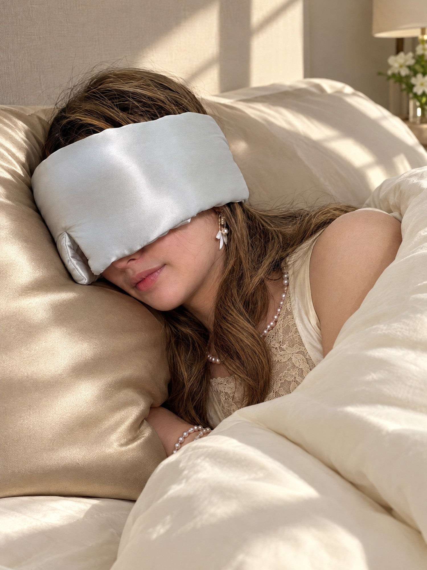 Debbie resting on the Mid9ight Dream Luxe mulberry silk pillowcase in Champagne, wearing the Deep Sleep eye mask in Moonlight